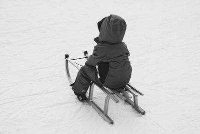 Rear view of boy sitting on sledge over snow covered field