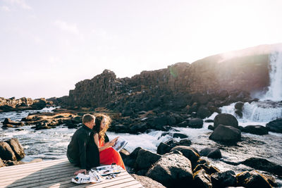 Man sitting on rock against sky