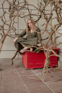 Portrait of woman sitting on box amidst bare trees