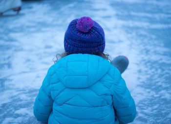 Rear view of girl sitting on snow covered field