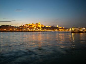 Illuminated city at waterfront during sunset