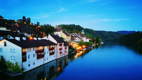 High angle view of illuminated buildings by river against blue sky