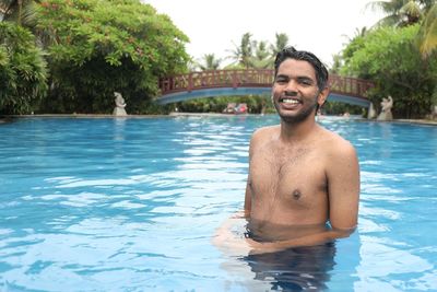 Portrait of shirtless smiling young man in swimming pool