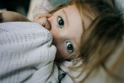 Close up portrait of young girl holding a comforter and sucking thumb