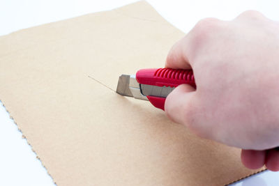 Close-up of hand cutting brown paper with utility knife on table