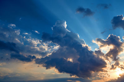 Low angle view of sunlight streaming through clouds