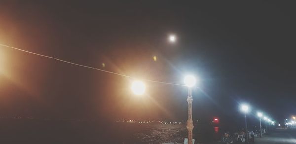 Illuminated street lights against sky at night