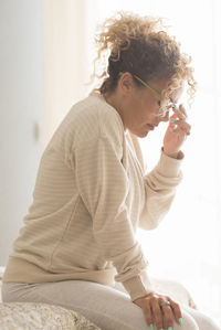 Side view of young woman sitting on bed at home