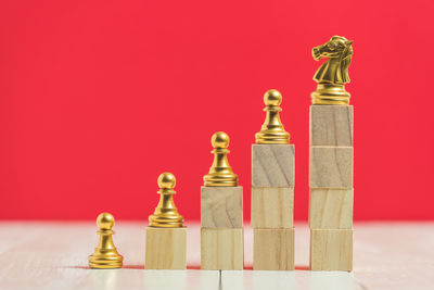 Close-up of stacked wooden toy blocks with chess pieces on table against red background