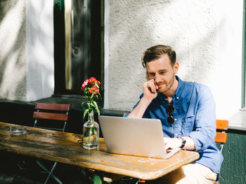 Young man using laptop while sitting by table