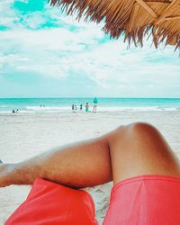 Low section of man relaxing on beach against sky