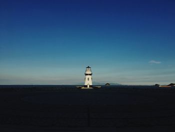 Lighthouse by sea against clear blue sky