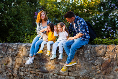 Full length of family sitting on wall outdoors