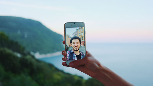 Man photographing using mobile phone against sky