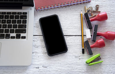 Directly above shot of smart phone and laptop with office supply on table