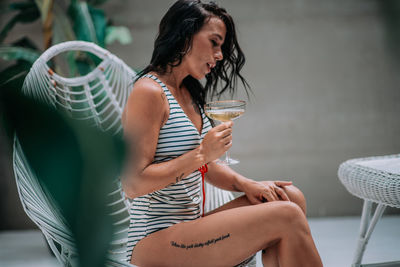 Midsection of woman drinking water from glass while sitting on chair