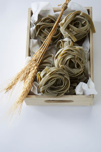 Close-up of pasta and stalks in crate against white background