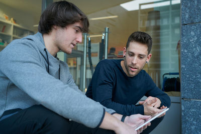 Front view of two young men talking sitting on a city staircase and lo