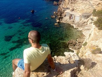 High angle view of man sitting on rocky mountains by sea