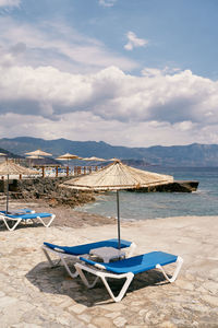 Deck chairs on beach against sky