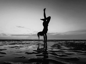 Silhouette woman with arms raised on beach against sky