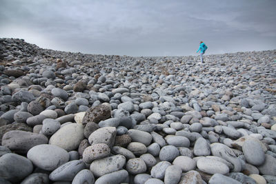 Full length of person standing on pebbles at beach against sky
