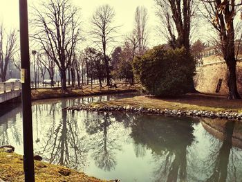 Reflection of bare trees in lake against sky in park