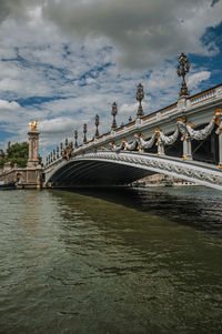 Arch bridge over river against cloudy sky