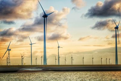 Wind turbines on land against sky during sunset