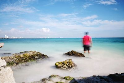 Rear view of man standing at beach against blue sky