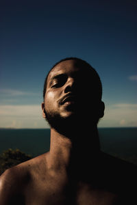 Portrait of shirtless man looking at sea against sky