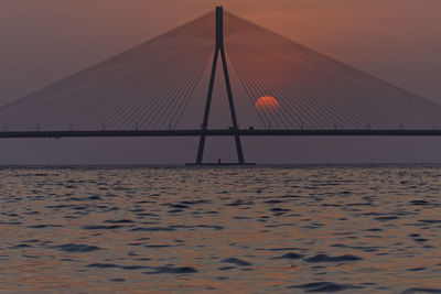 Suspension bridge over sea against sky during sunset