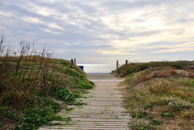 Footpath leading towards sea against sky