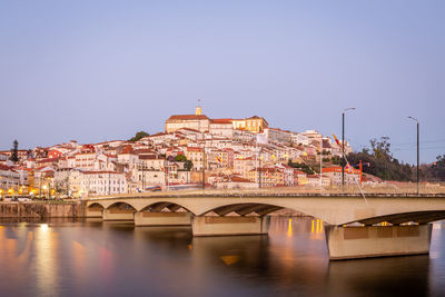 Arch bridge over river by buildings against clear sky