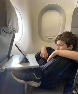 Little boy relaxed traveling by plane. child sitting by aircraft window and using a digital tablet