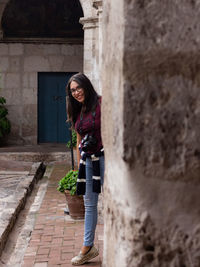 Full length portrait of smiling young woman standing by wall