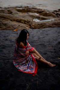 Young woman with shawl sitting on black sand beach