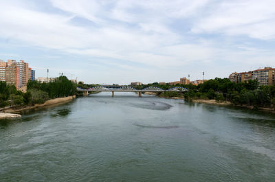 Bridge over river by buildings against sky