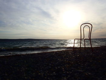 Old chair on beach against sky during sunset