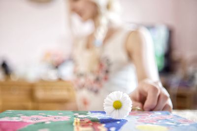 Woman holding white daisy by table