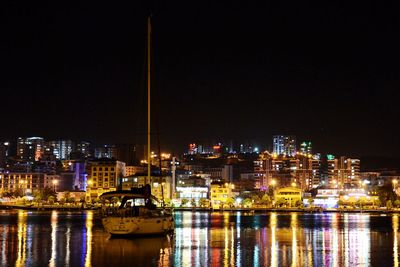 Illuminated buildings by river against sky at night