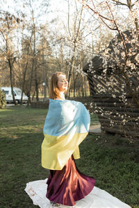Woman in dress with ukranian flag near trees in spring park