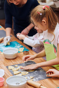 Midsection of woman assisting girls in making cookies on table