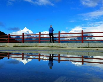 Man standing on railing against blue sky
