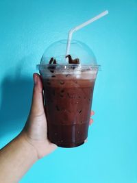 Cropped image of hand holding drink against blue glass