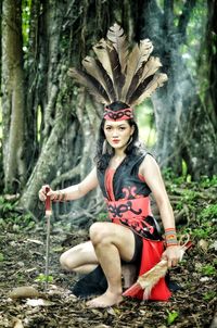 Portrait of young woman wearing costume crouching by tree in forest