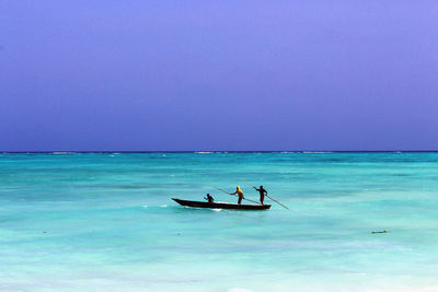 Men in boat on sea against clear blue sky