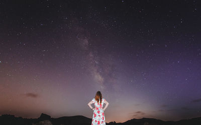 Rear view of woman standing against sky at night