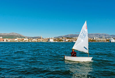 Sailboat sailing on sea by buildings against clear blue sky