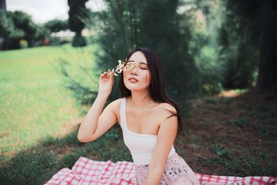 Smiling young woman holding flowers while sitting against trees in forest